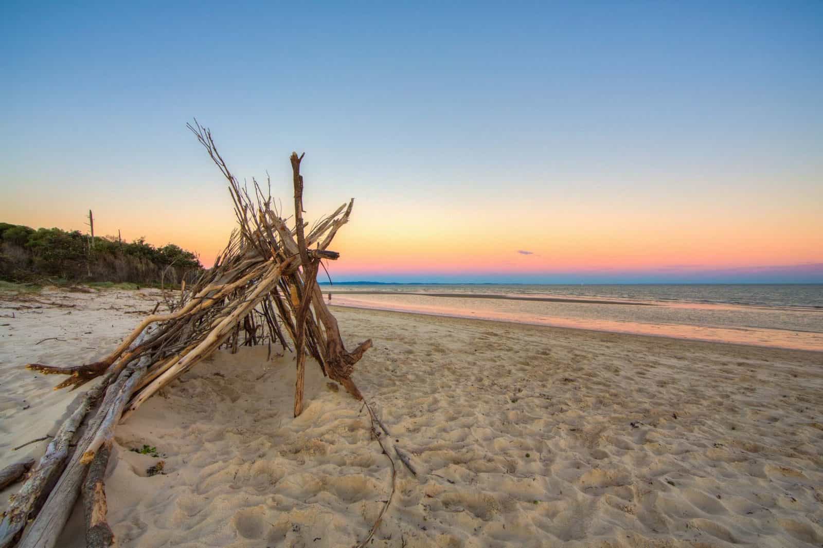 Large triangular tent made out of sticks and branches on the beach at sunset