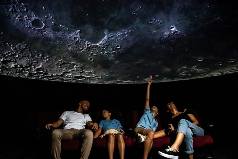 Family seated in a Planetarium theatre looking up at a Moon image