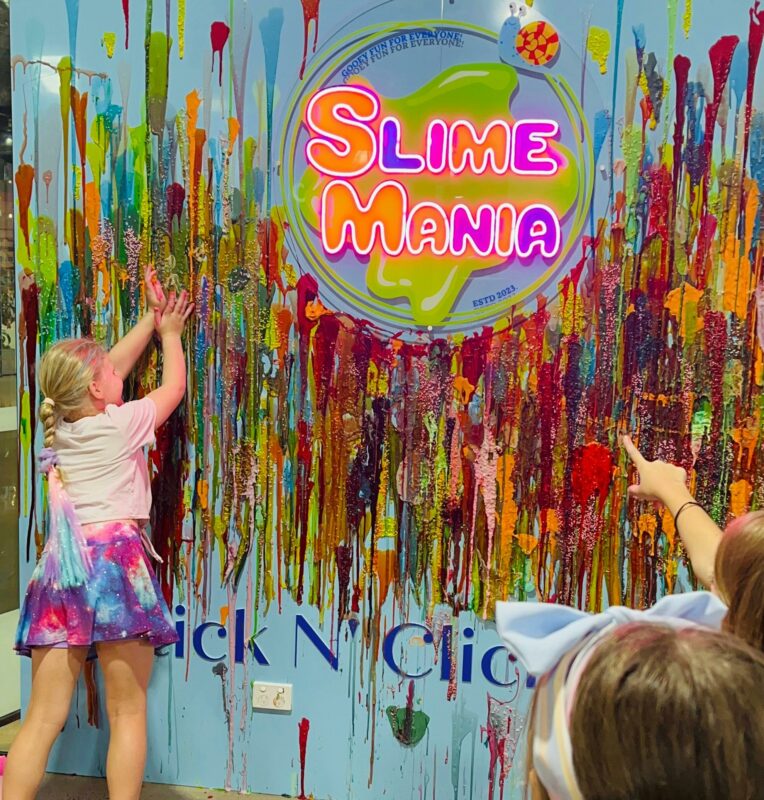Slime wall where we have a Slime Mania logo and there is a girl sticking her favourite slime.