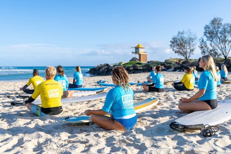 Surf school group meditating on beach.