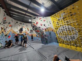 A lot of climbers standing on the climbing mat with some people climbing on the wall at Wall Walkers