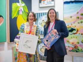 Two friendly gallerists at their Affordable Art Fair stand holding an artwork each