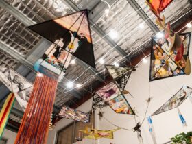 A series of colourful handmade kites adorn the ceiling of a gallery space.