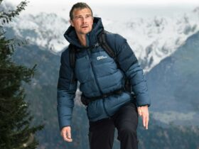 Bear standing in front of a snowy mountain wearing a blue puffer jacket and black pants