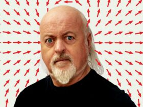 Bill Bailey behind a white background with red arrows pointing to him with a shock look on his face