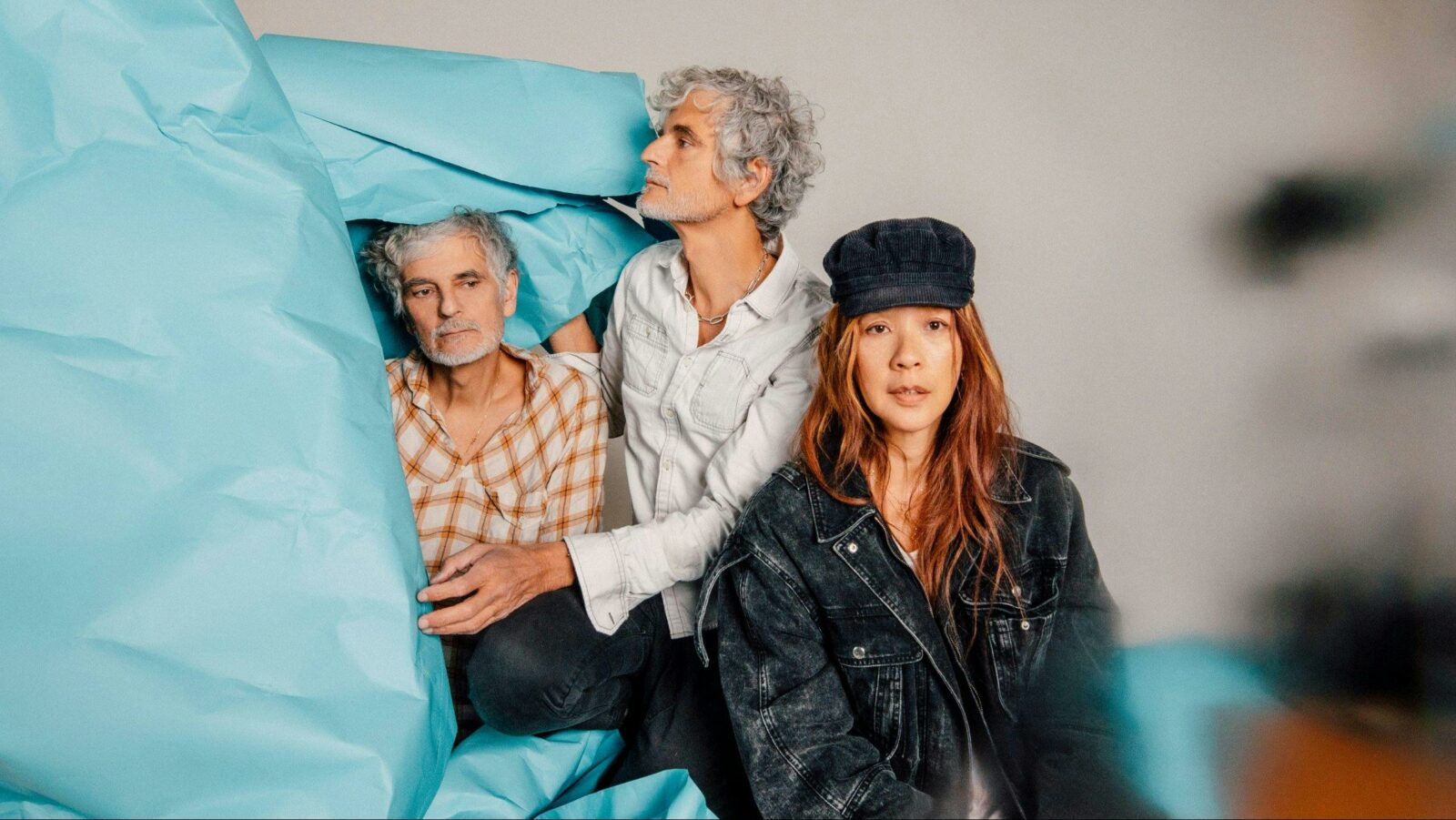 Blonde Redhead - 3 people photographed sitting with a coloured piece of paper draped to the left