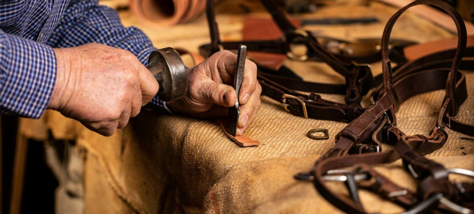 A pair of hands, using tools to put a hole in a leather piece for a horse bridle.