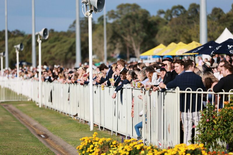 Crowd standing along the fence line watching the horses run