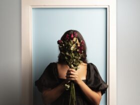 Girl stands in front of a blue door with dead flowers covering face