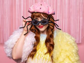 A character in a pink and yellow sparkly dress wearing funky sunglasses that look like a spider.