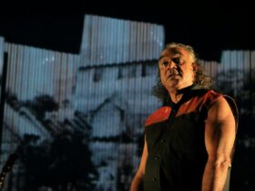 An Indigenous man stands on stage with corrugated iron backdrop.