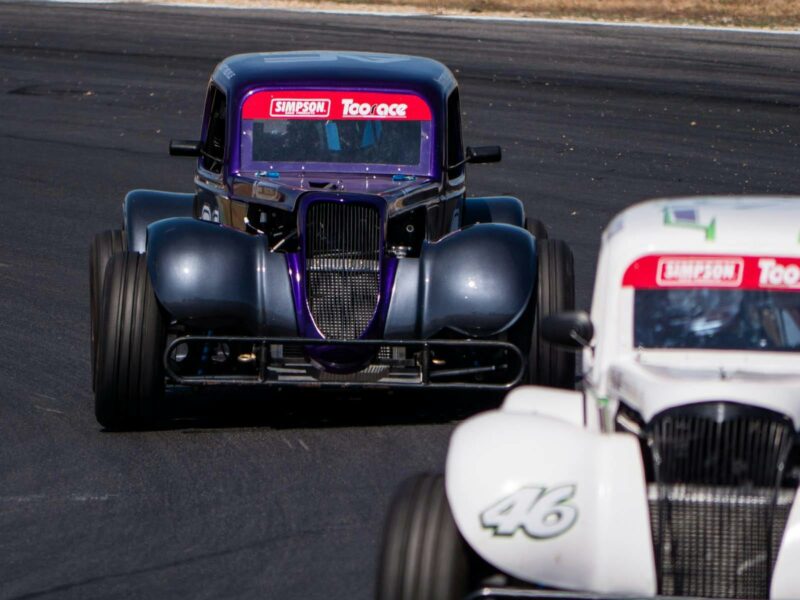 Two white and black legend cars racing around a racetrack