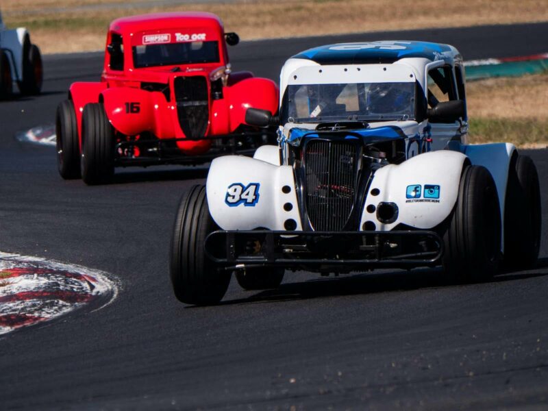 One white and one red legenda car on a racetrack
