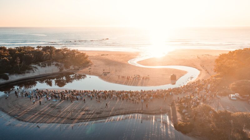 Drone footage of people gathered on a beach watching a performance at dawn