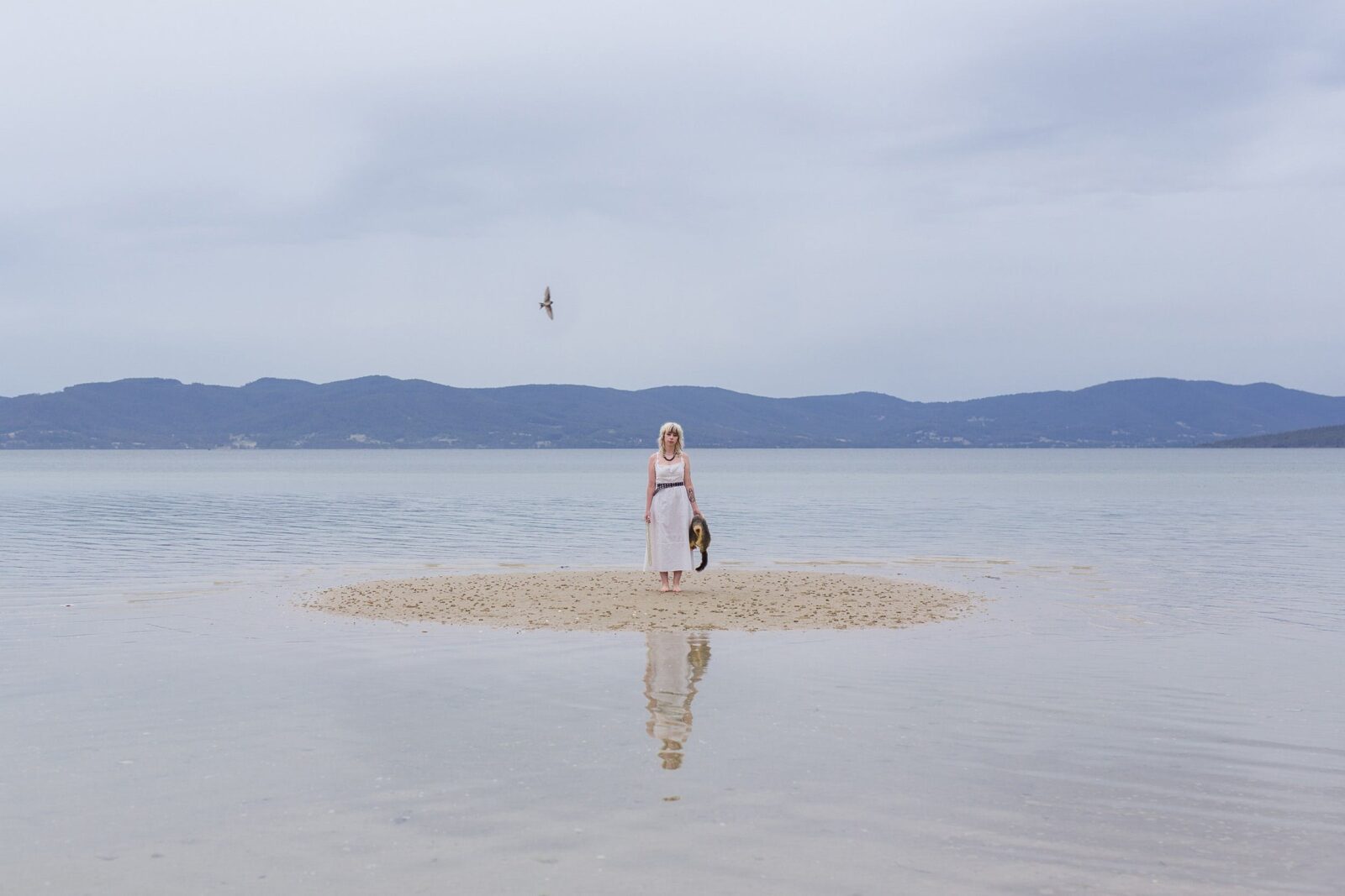 A woman standing on a patch of sand in a shallow lake.