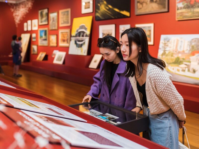 Two young adults inspect didactics and pull-out drawers in a gallery space with dark-red walls.