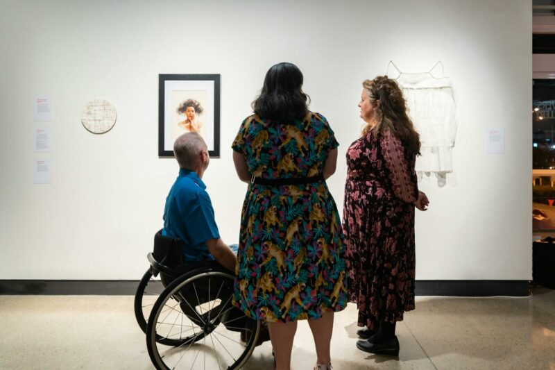 Three people standing in front of a few small artworks.