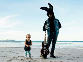 Small boy beside a man in a bunny suit with guitar at the beach