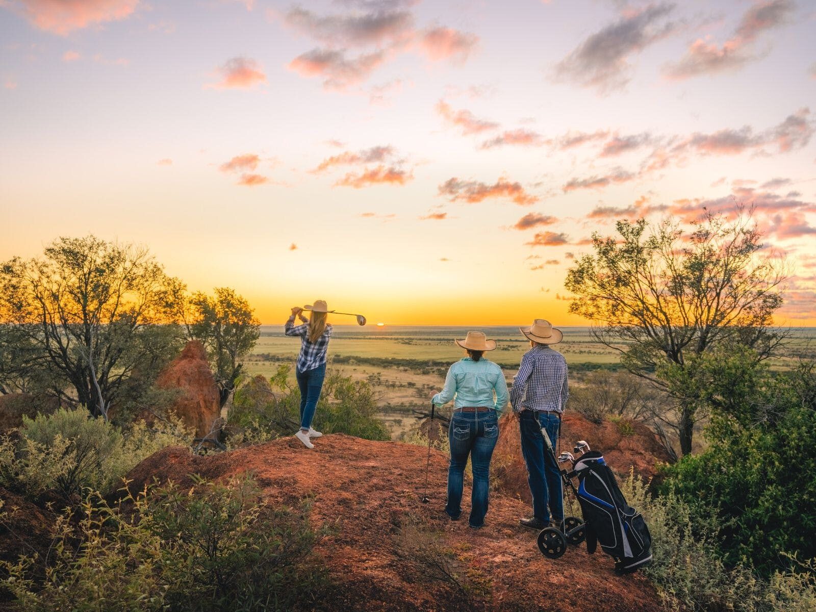 Female golfer tees off from Jump Up in Winton Outback Queensland with two golfers watching on.