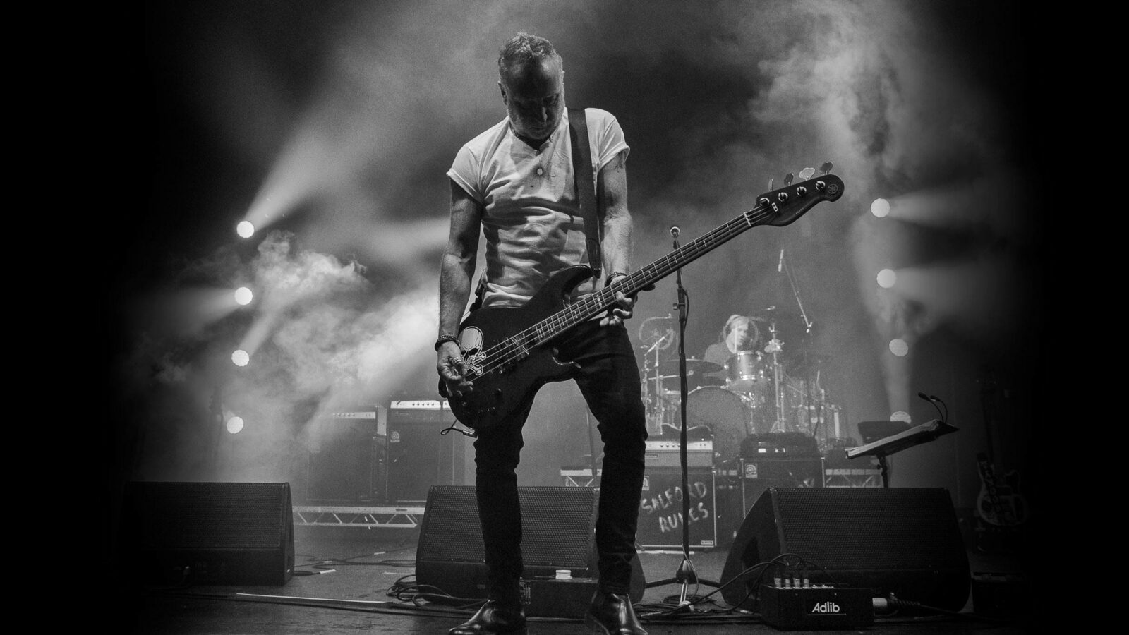 Peter Hook & The Light - person playing guitar on a stage with rest of band behind them