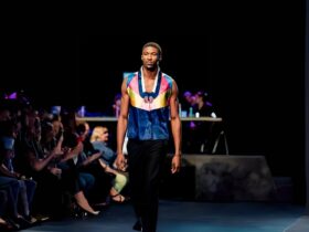 A man in a vibrant vest struts down a runway, exuding confidence and style.