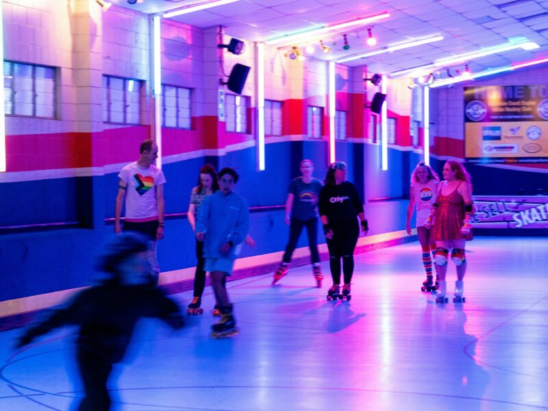 A group of people in the foreground and back ground skating at a colourfully lit rink