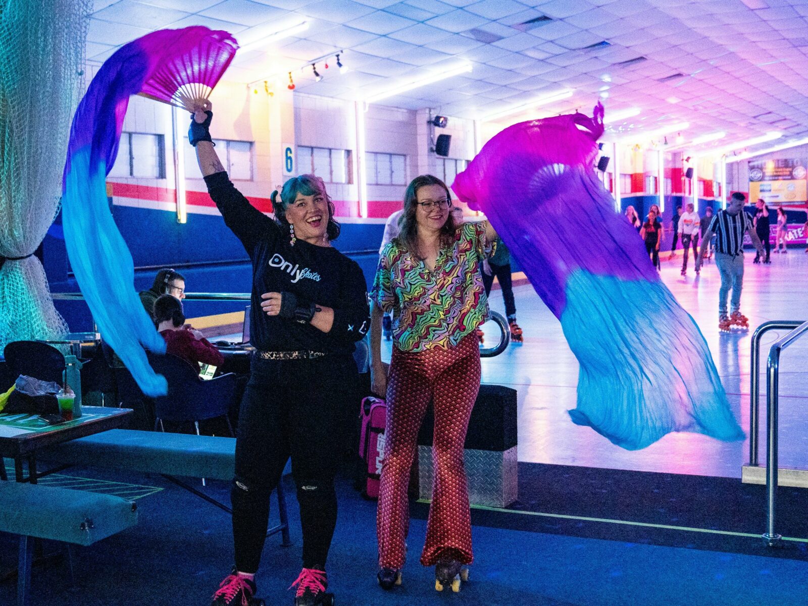Two people waving colourful silks near a skate rink