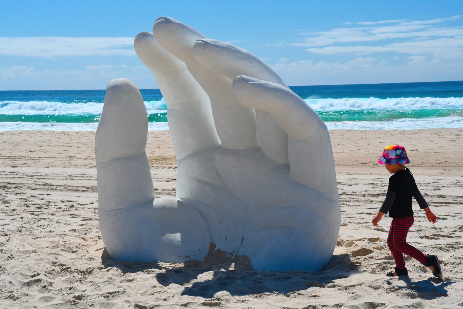 A giant hand gently reaching out of the sand, sitting at 2.4m high, conveying openness and trust.