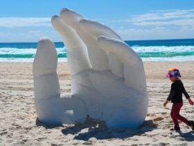 A giant hand gently reaching out of the sand, sitting at 2.4m high, conveying openness and trust.