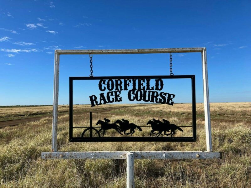 A metal cutout sign saying Corfield Race Course with open grass downs background