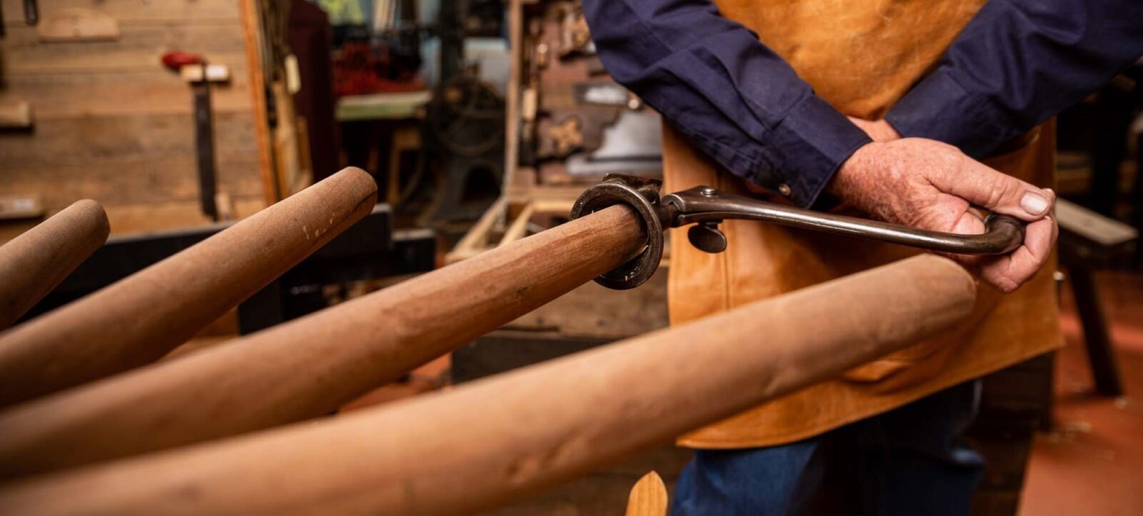 A wood worker using a hand tool to shape the spoke of a wagon wheel.