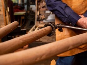 A wood worker using a hand tool to shape the spoke of a wagon wheel.