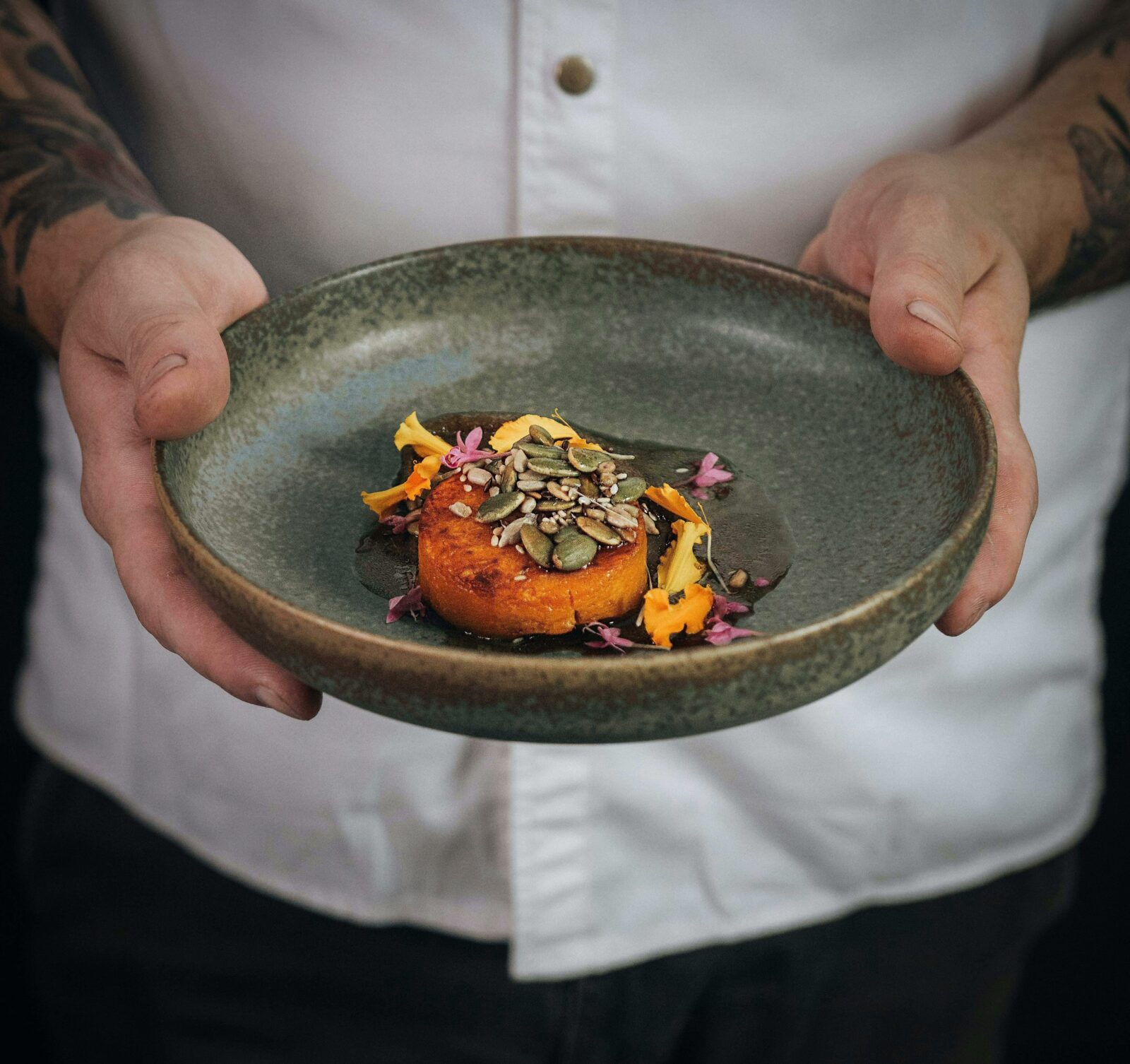 Alan holds a green plate with local roasted pumpkin, seed puree and flowers