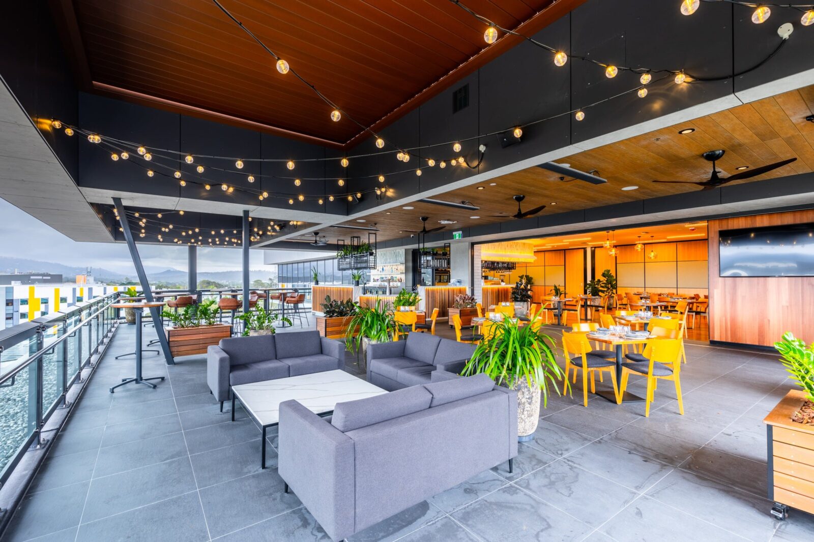 Rooftop area with lounges and tables, festoon lights and hinterland views