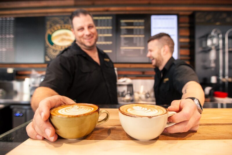 Two men holding up lattes to camera