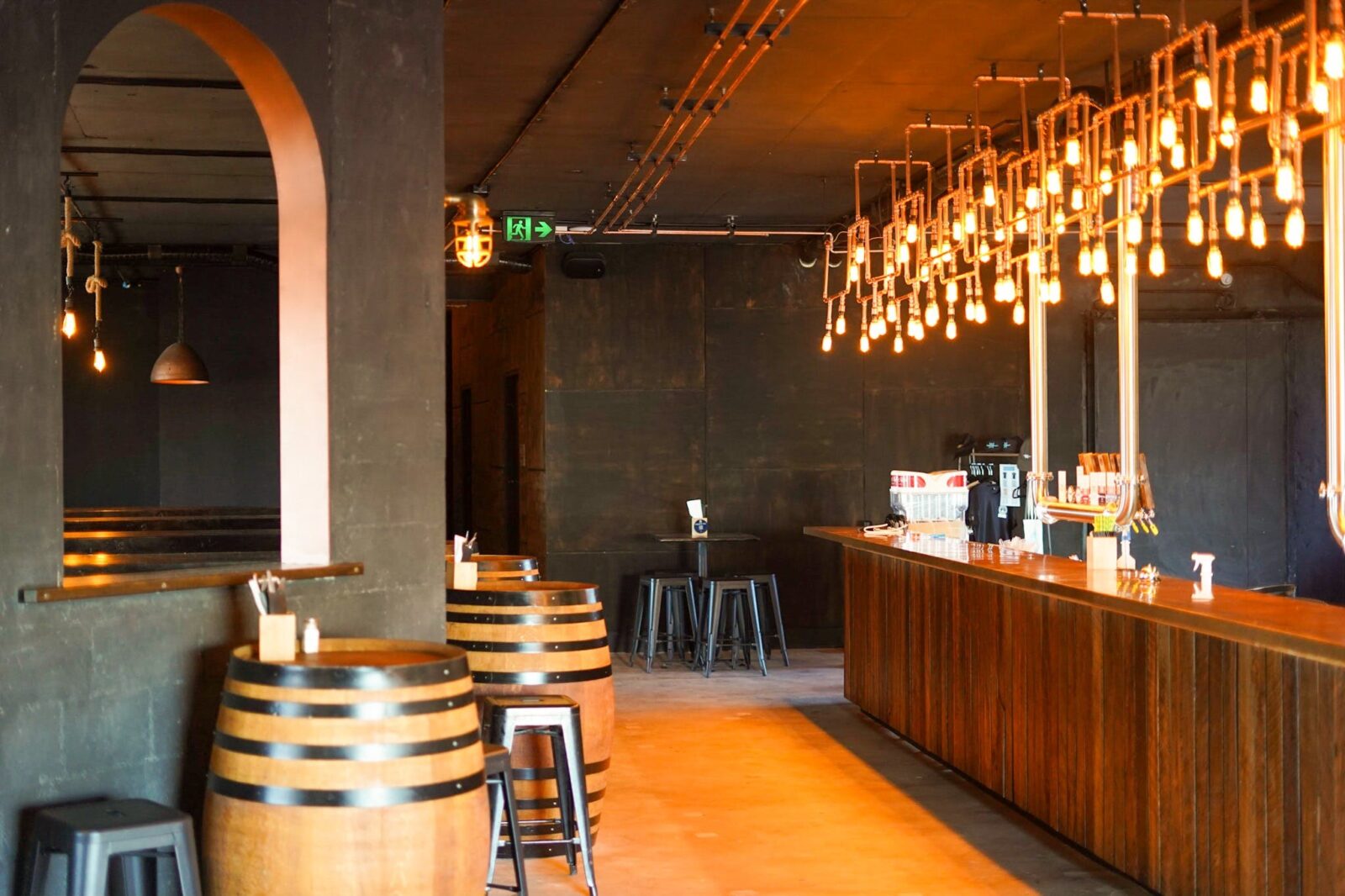 Copper lights above a copper and timber long bar. Wine barrels and seats in front of archways
