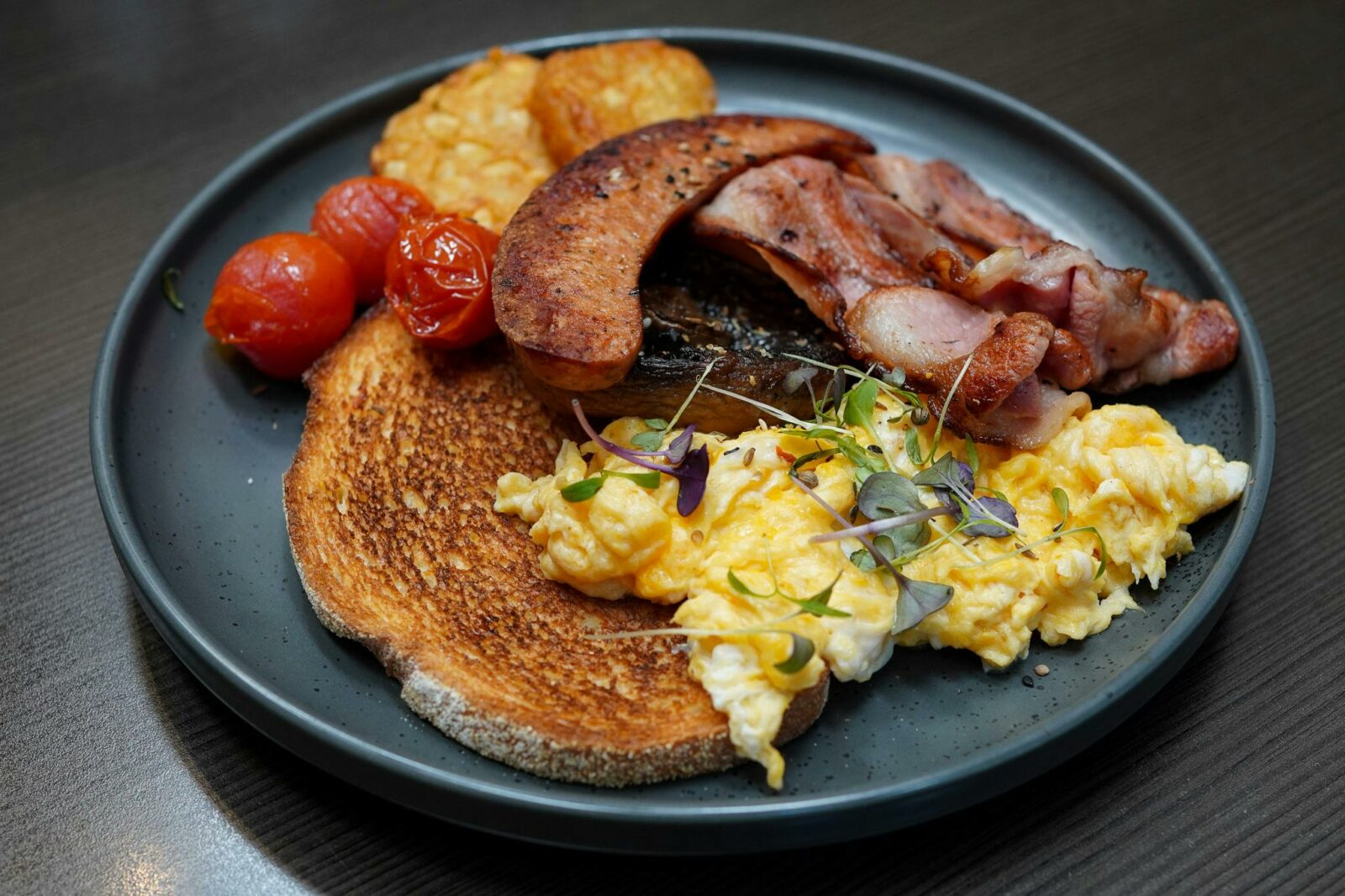 A breakfast order with bacon, sausage, scrambled eggs, hash browns, tomatoes and toast