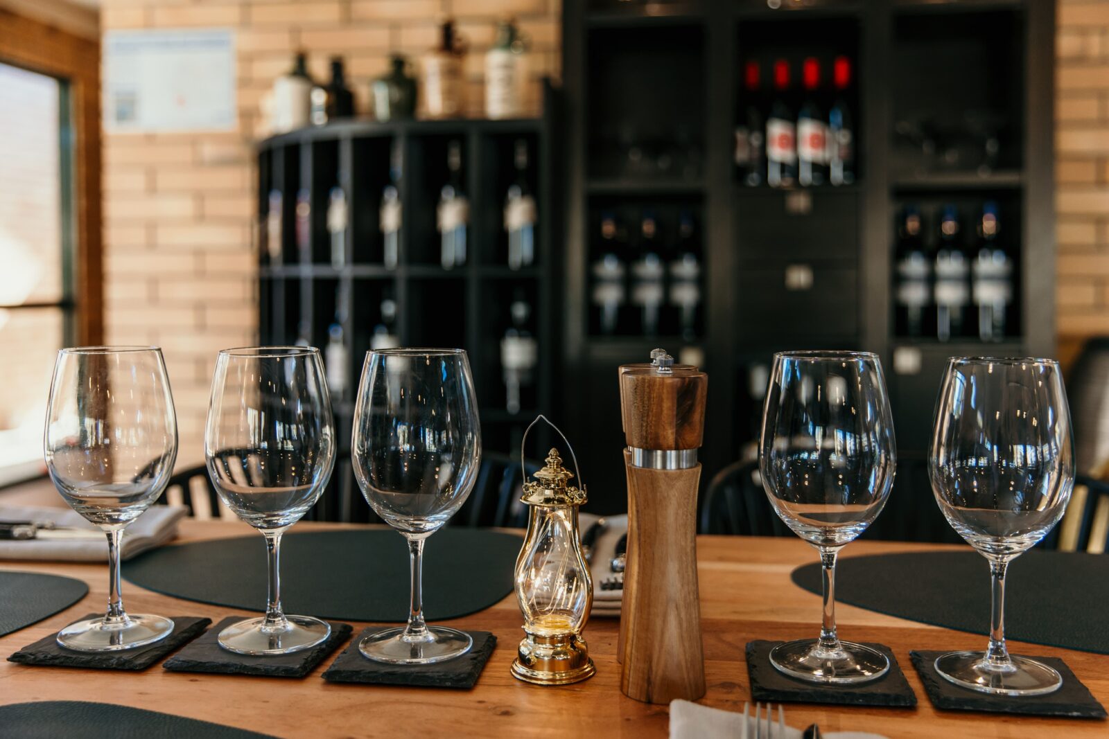 A set table in a restaurant with glassware, and a wine rack in the background.