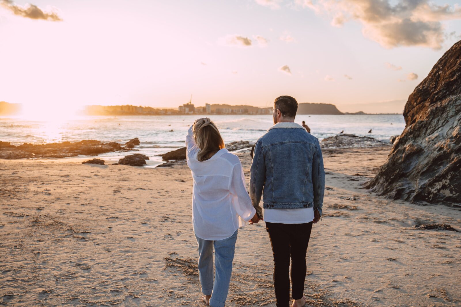 A couple holding hands, walking along a beach towards a sunset