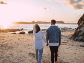 A couple holding hands, walking along a beach towards a sunset