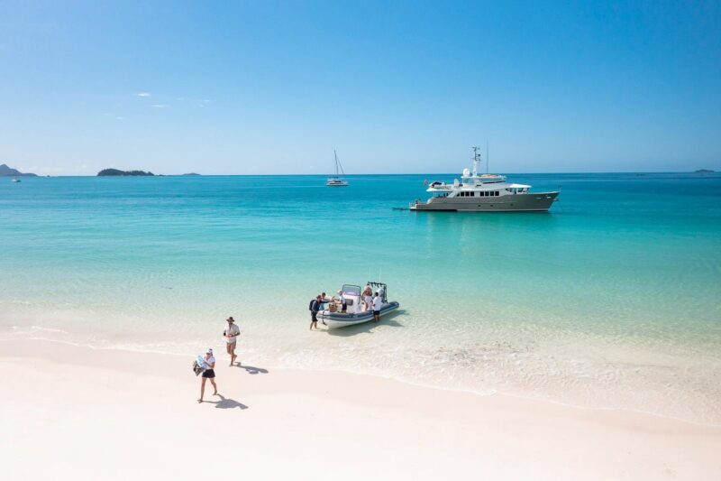 Passengers stepping onto Whitehaven Beach in Whitsundays with Texas T motor yacht in background