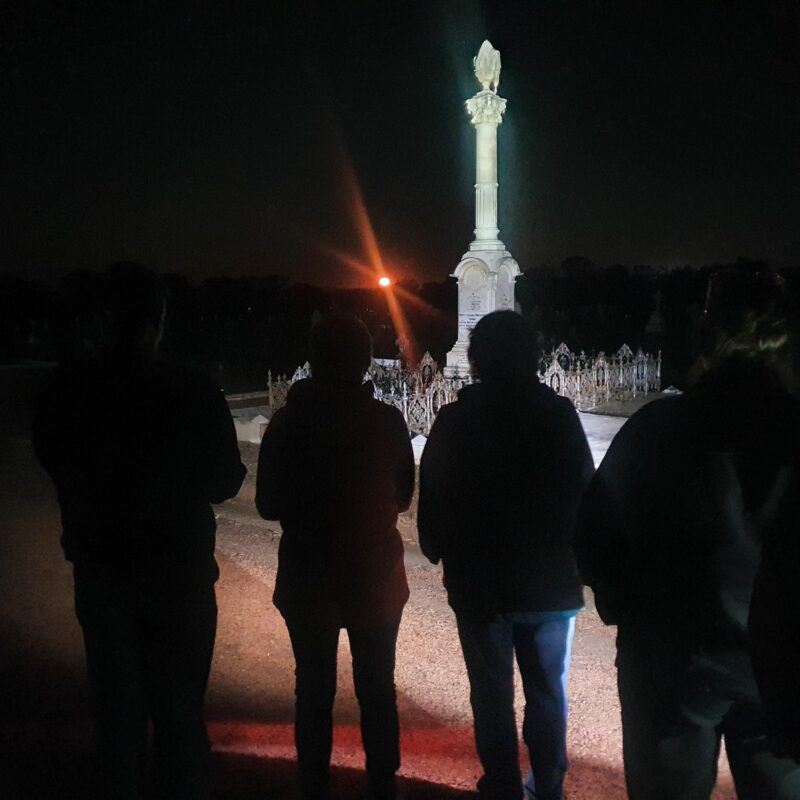 silhouette of group of 4 people standing in front of graveyard statue