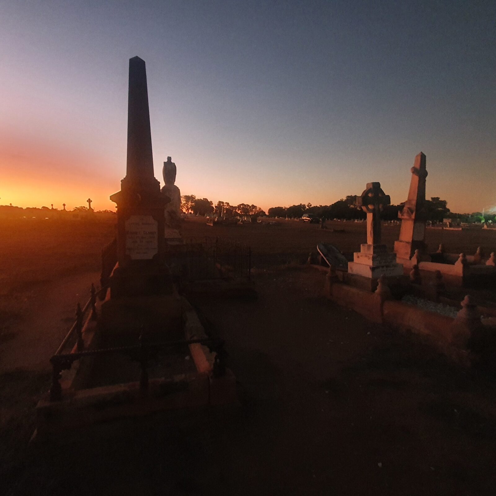 Charters Towers Cemetery with a few grave statues and thesun setting in distance