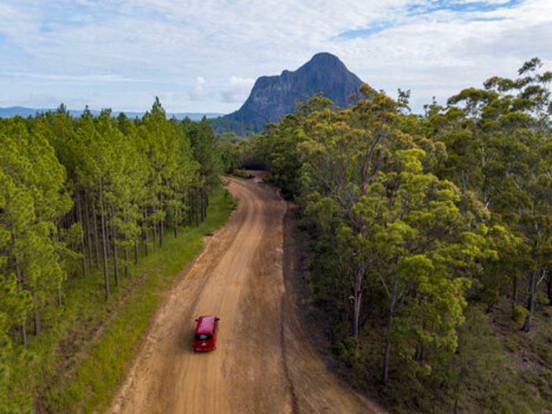 Image shows the tour bus driving on a dirt road with Mt Beerwah in the background
