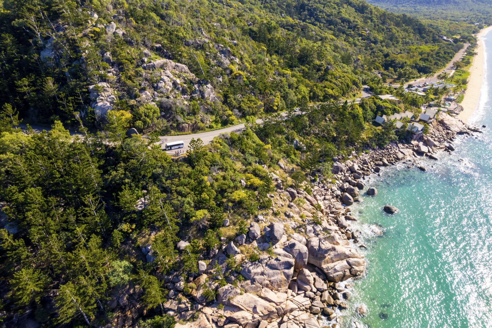 Drone shot of tour bus travelling a mountainside road, overlooking oceans