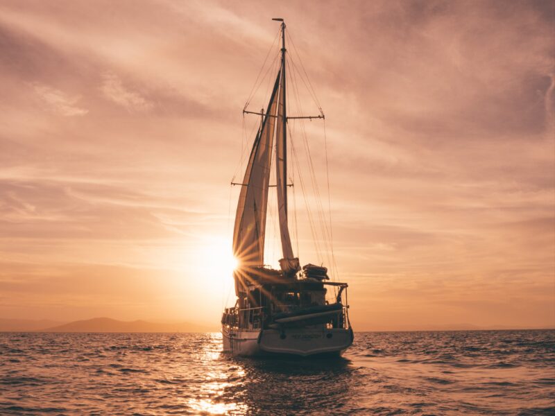 A sail boat, sailing towards the sunset on the horizon