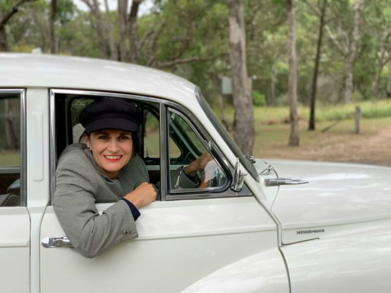 Woman smiling, looking out open car window, wearing a hat
