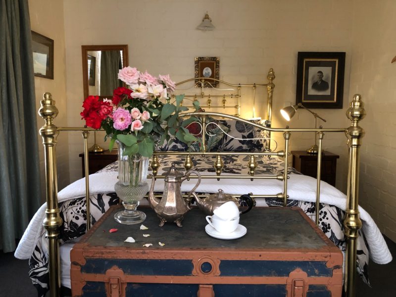 A Queensize brass bed in a cottage bedroom with old photos and fresh flowers and silver tea pots