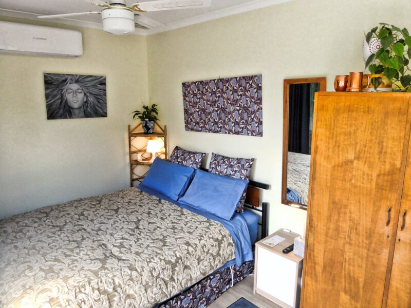 Comfortable queen bed, with aqmple pillows, bedside tables, artwork, and wardrobe.