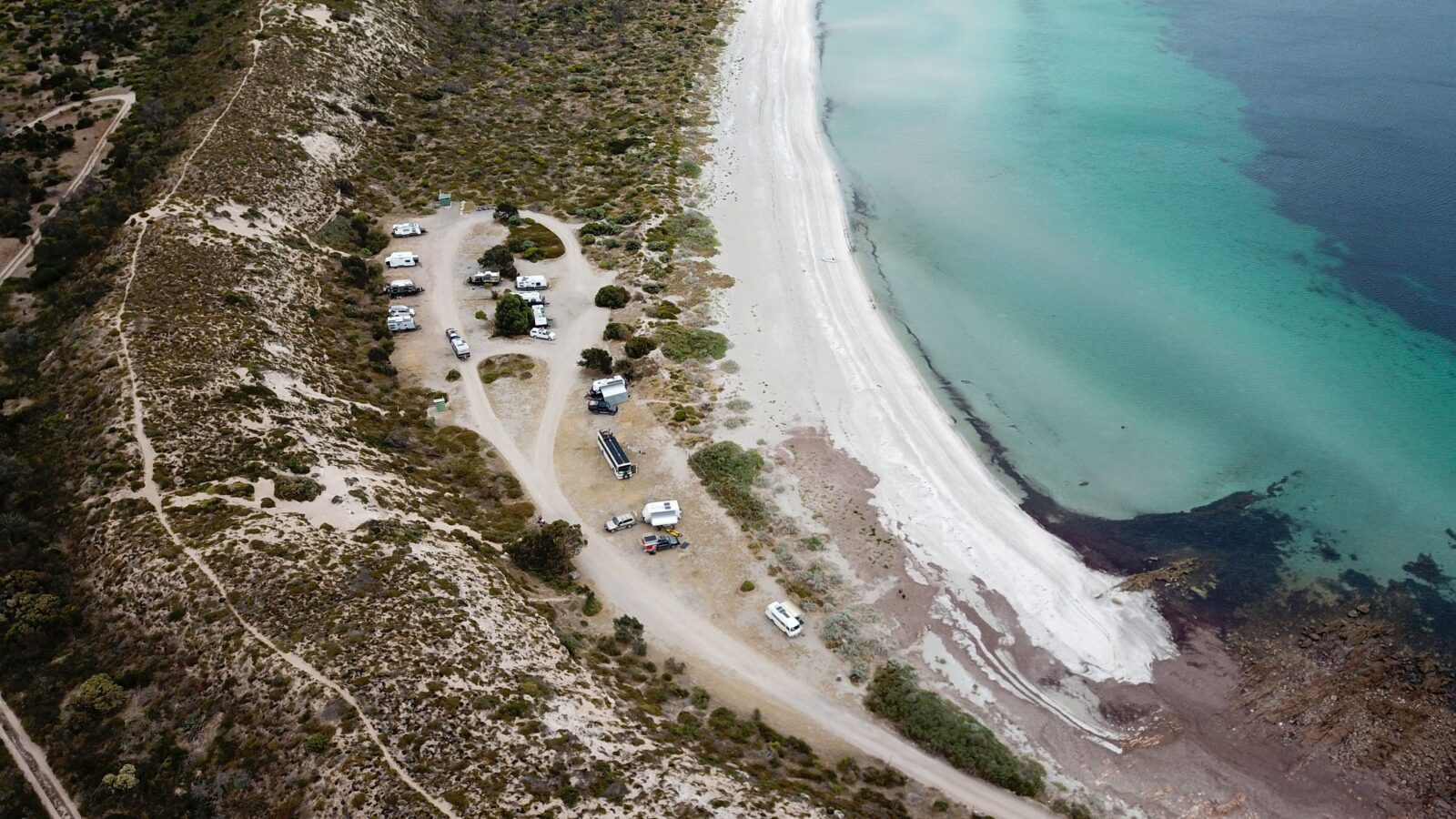 Drone view of campground alongside white sand and turquoise water
